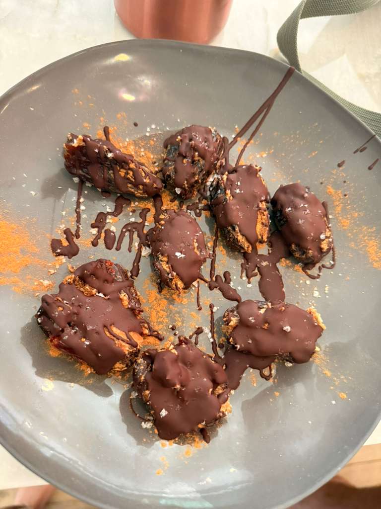 Chocolate peanut butter stuffed Medjool dates topped with melted chocolate, ground cinnamon, and flaky sea salt on a gray plate.