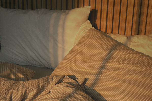 Bed and pillows in soft evening light representing rest, sleep, and recovery after a busy day.