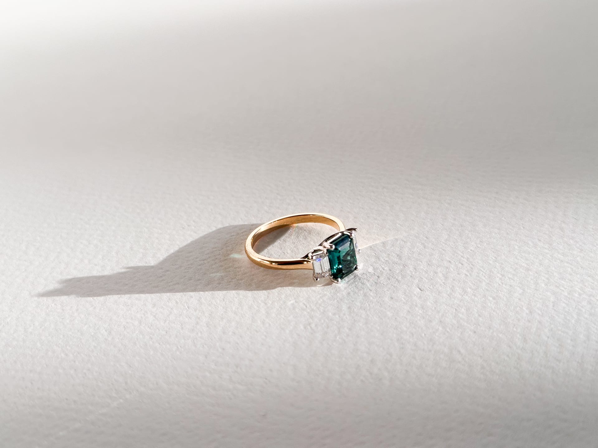 3 Stone Emerald Gemstone Emerald Cut Diamond Engagement Ring with accenting diamonds in a yellow gold band