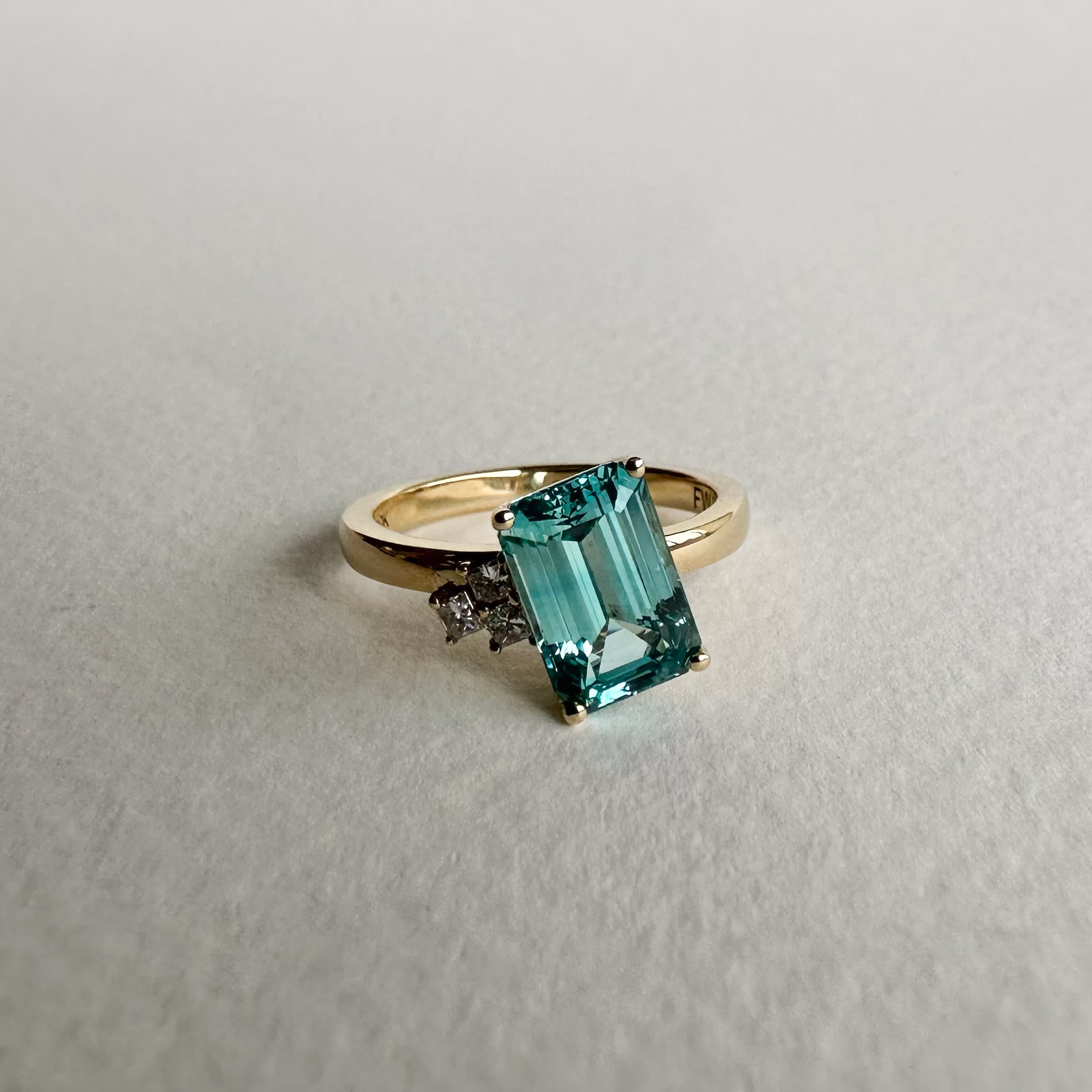 Asymmetrical teal sapphire with accenting diamond stones in 14K yellow gold