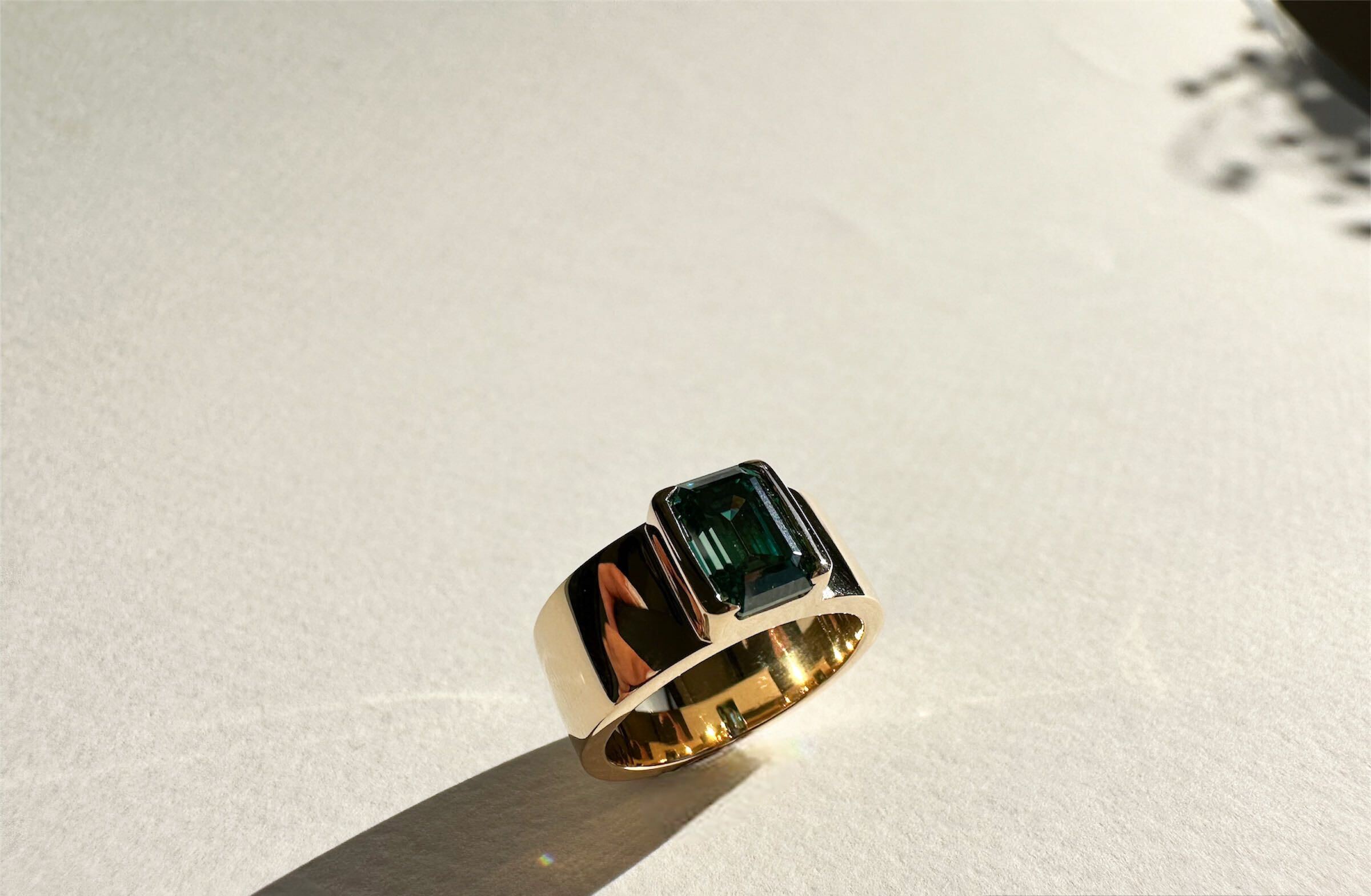 Emerald cut green sapphire with half bezel in a yellow gold band