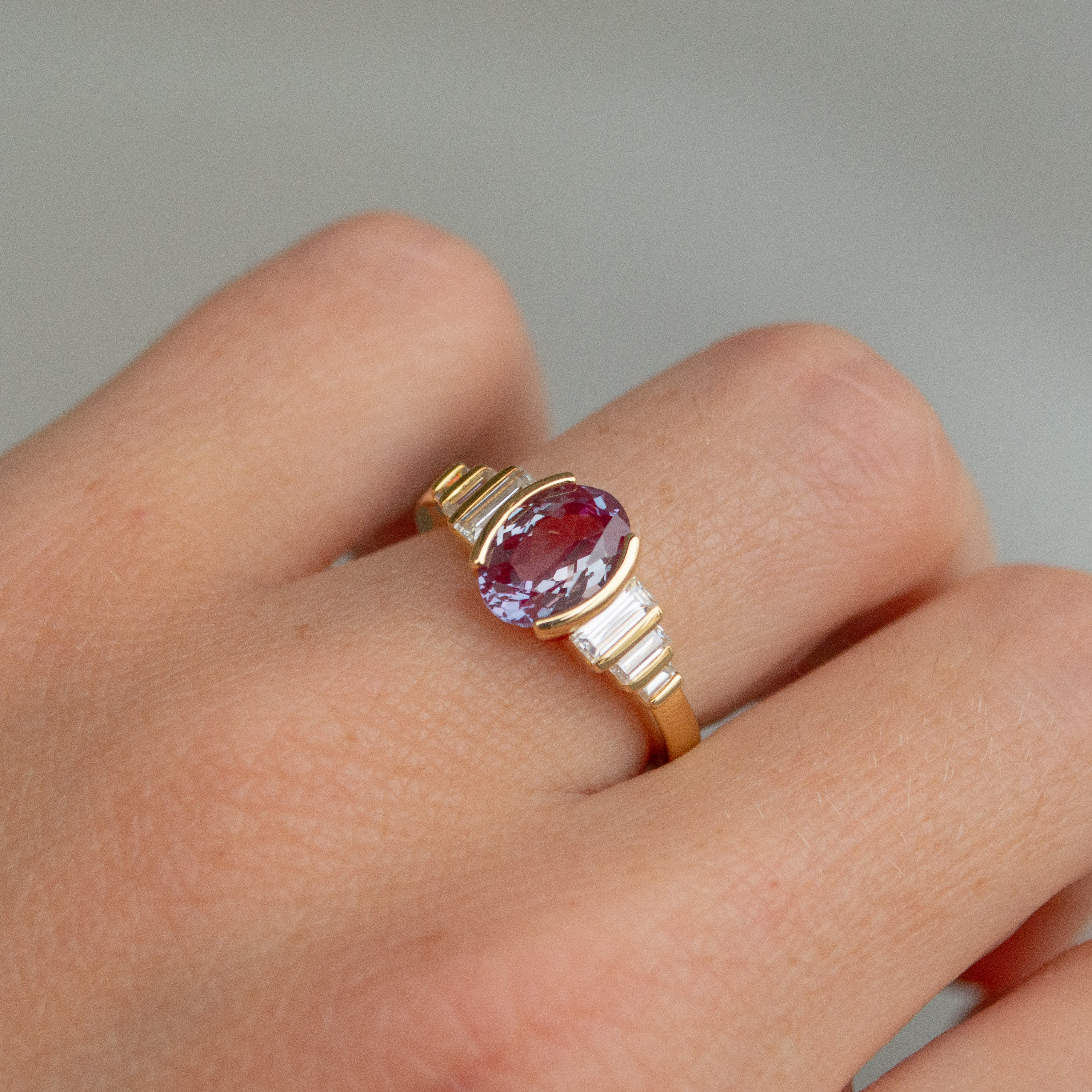 Red alexandrite in an oval cut featuring an accordion of emerald cut diamonds in 14K yellow gold