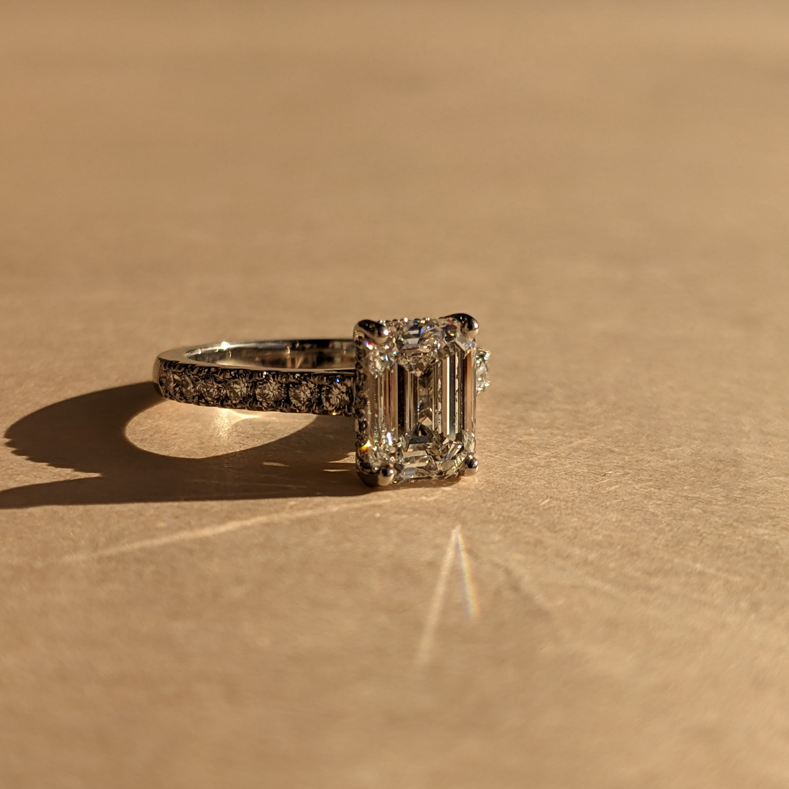 Emerald cut diamond solitaire engagement ring with pave set diamonds half way along the platinum band