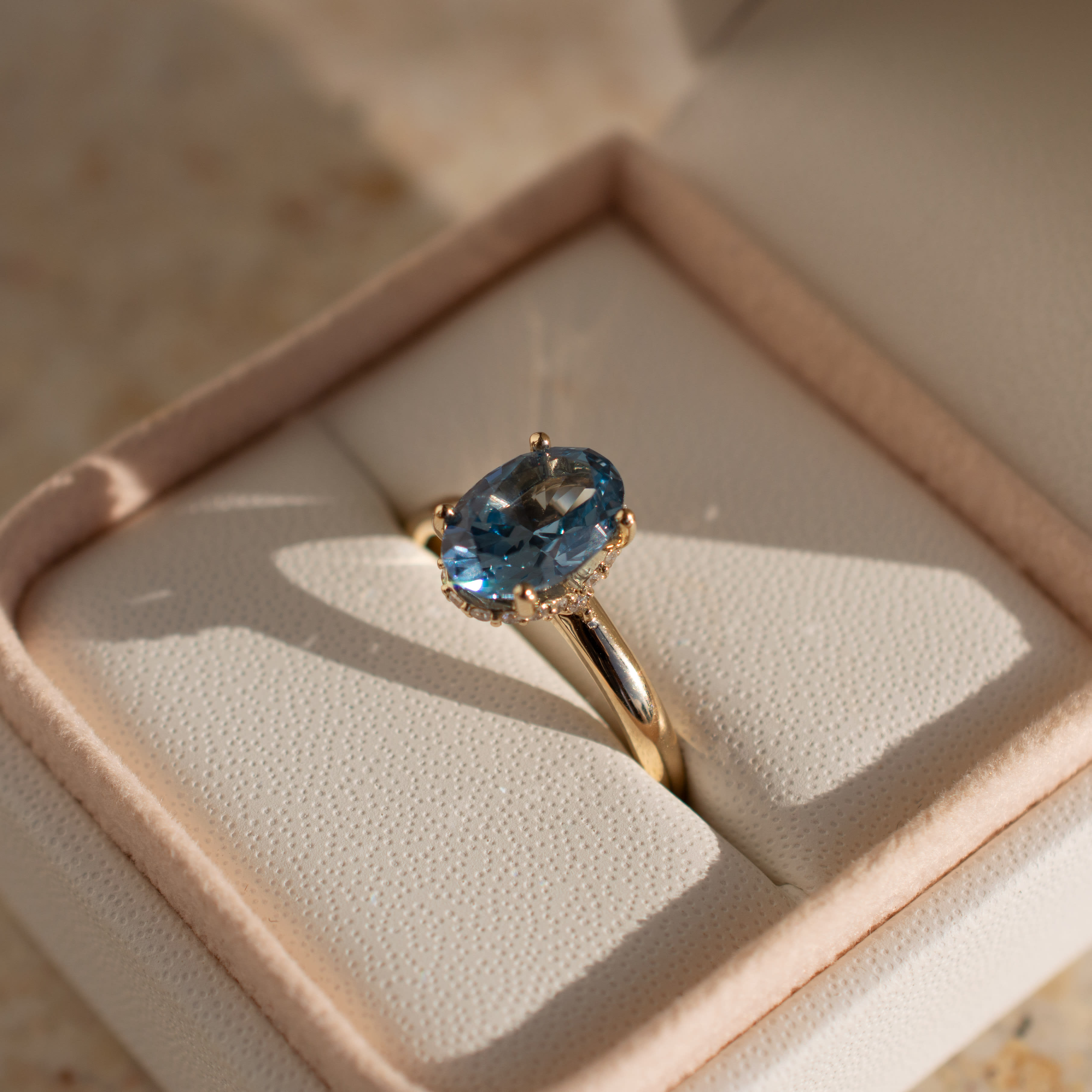 Oval sapphire engagement ring with round prongs, hidden halo and in a yellow gold band. 