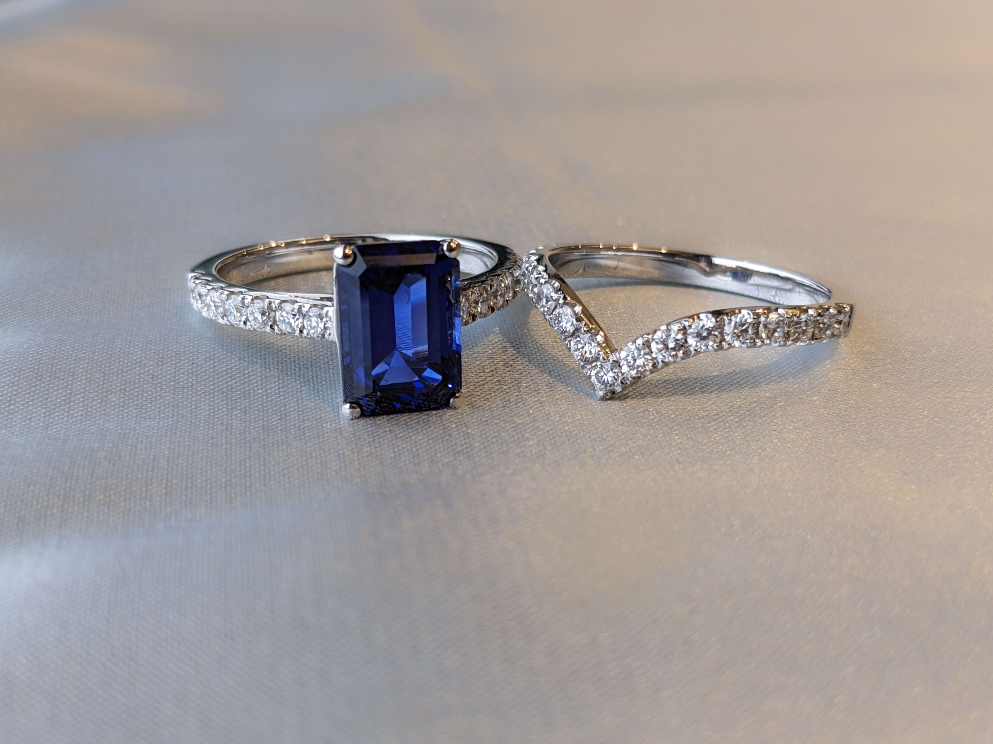 Bridal set featuring a 1.5 carat emerald cut blue sapphire engagement ring with pave diamonds in a platinum band and a curved wedding ring also with pave set diamonds.