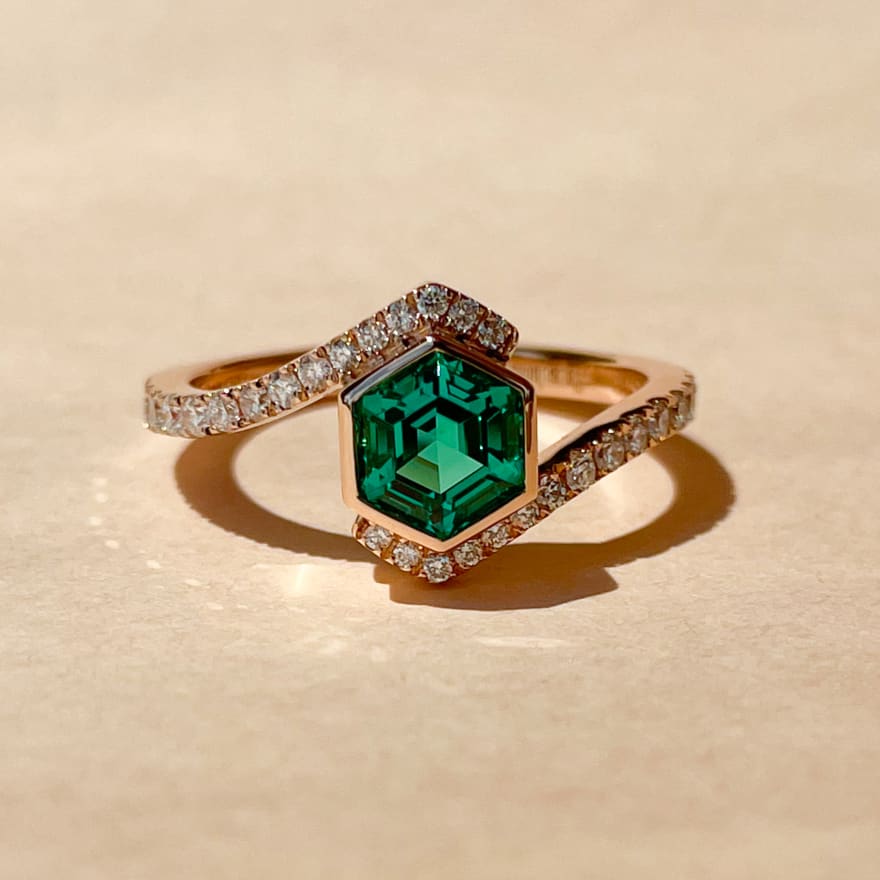 Hexagonal cut green emerald in a 14k yellow gold band with pave diamonds
