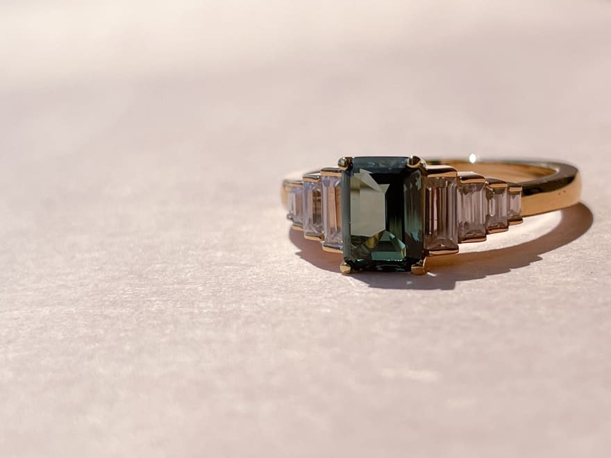 9 stone engagement ring featuring an emerald cut emerald and 8 accenting diamond stones in a 14k yellow gold band