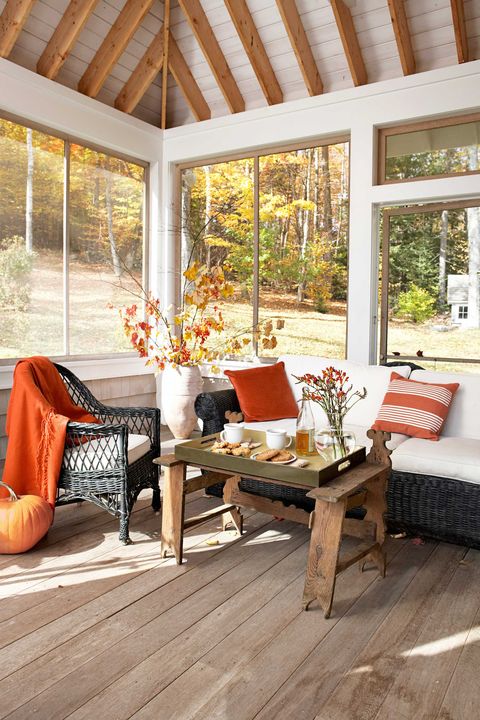 Wicker pieces, accented with burnt-orange accessories, offer to seat on this glassed-in porch - Fall Decorating Ideas