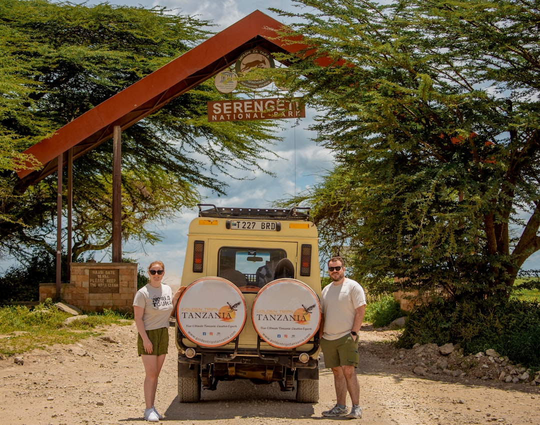 Two people with a safari vehicle under a serengeti archway.