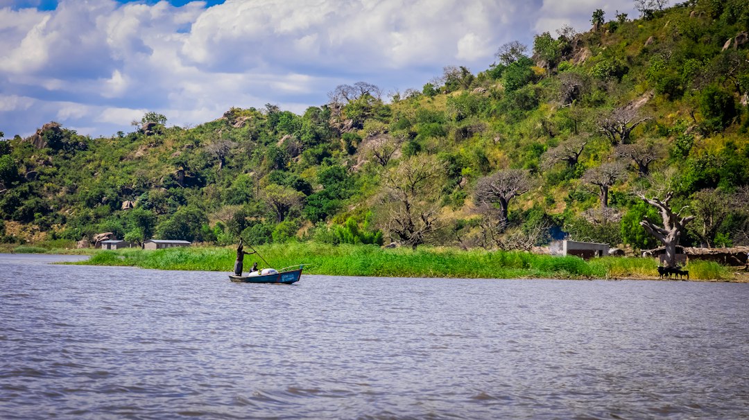 a small boat floating on top of a river next to a lush green hillside
