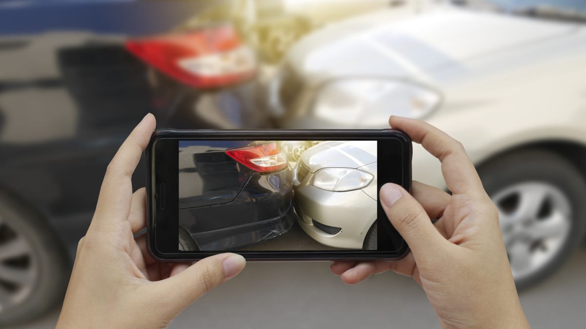 Persona fotografiando un vehículo con su teléfono móvil después de un siniestro