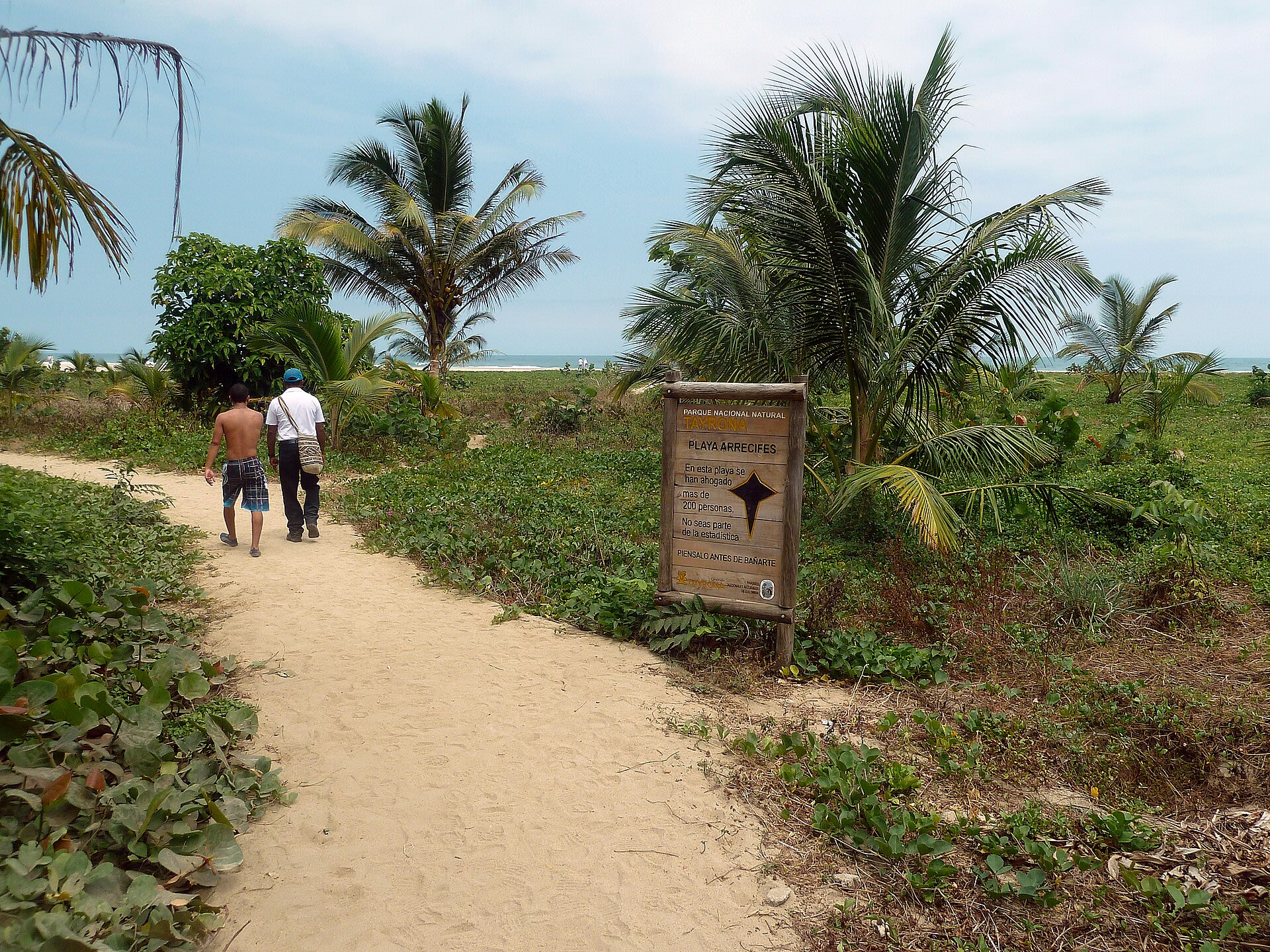 Sendero de arena hacia Playa Arrecifes con el cartel de Parques Nacionales que advierte sobre ahogamientos