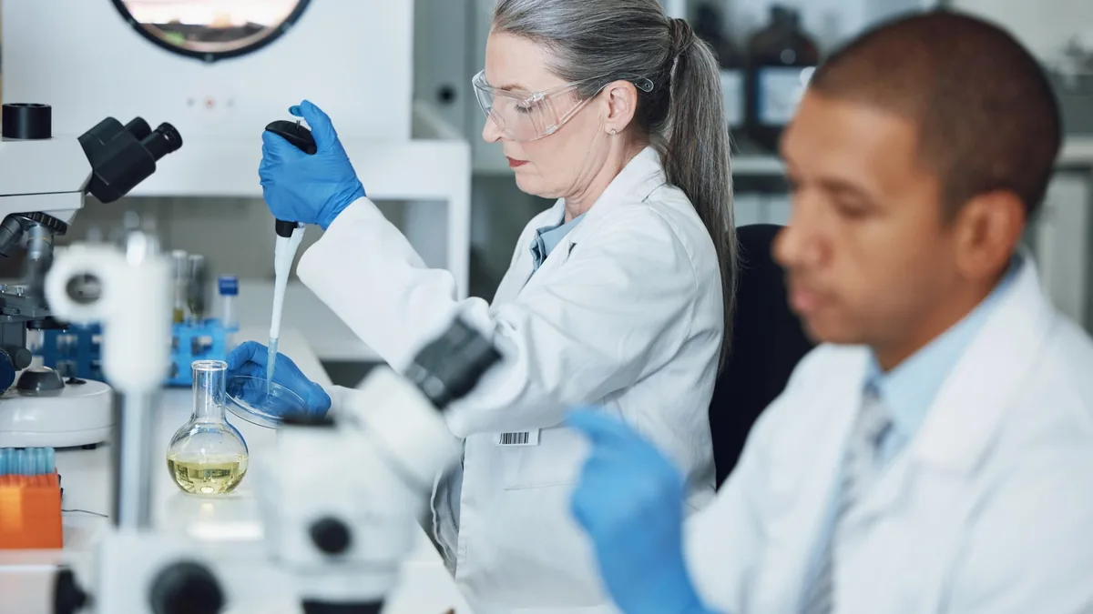 Investigadores con bata y guantes azules que trabajan con microscopios y pipetas en un laboratorio