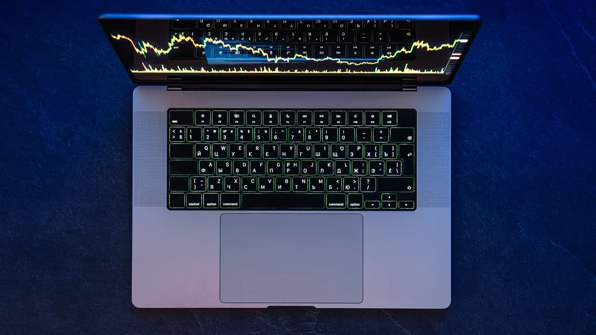Laptop vista desde arriba con una gráfica de cotizaciones en la pantalla, sobre una mesa azul