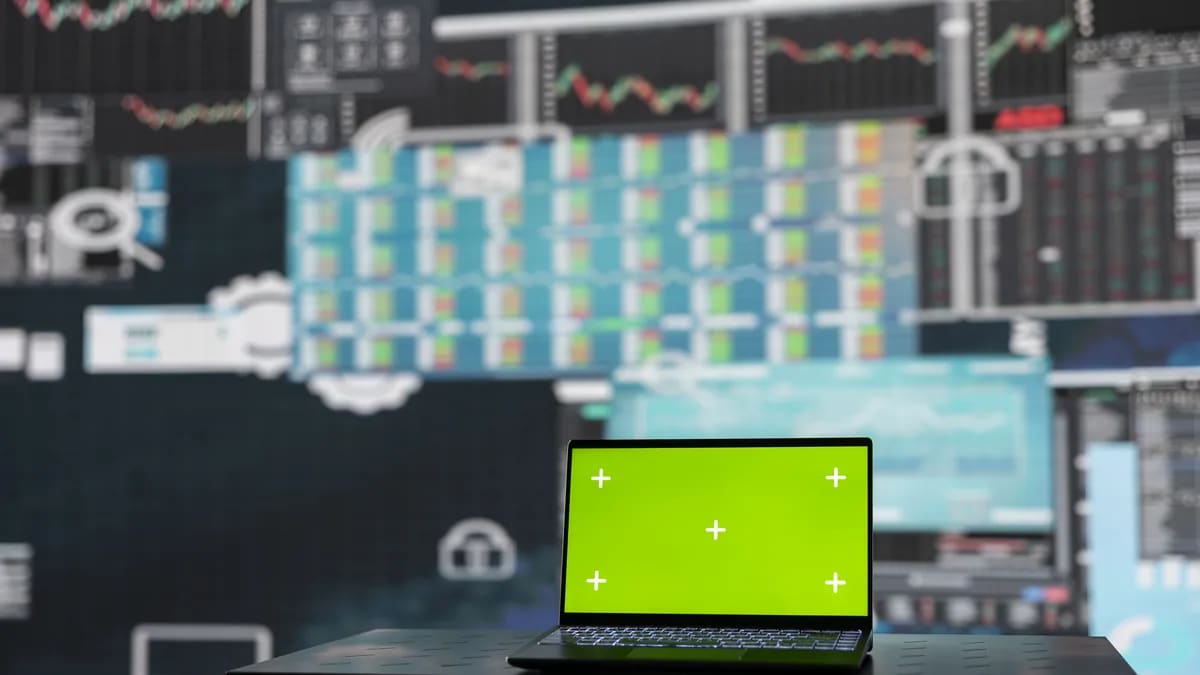 Laptop con la pantalla en verde frente a un muro de pantallas con gráficas y tablas