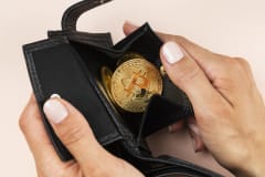 Manos que abren una cartera negra con una moneda de Bitcoin adentro