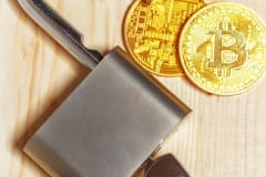 Monedas doradas de Bitcoin junto a un candado sobre una mesa de madera