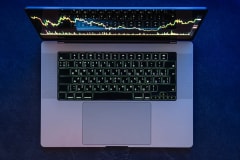 Laptop vista desde arriba con una gráfica de cotizaciones en la pantalla, sobre una mesa azul
