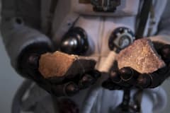 Manos con guantes que sostienen dos trozos de mineral rojizo