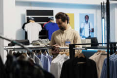 Hombre que revisa una tableta en una tienda de ropa con camisas en exhibición