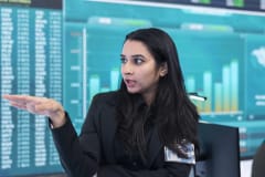 Mujer que explica gráficas de barras proyectadas en una pantalla de datos financieros
