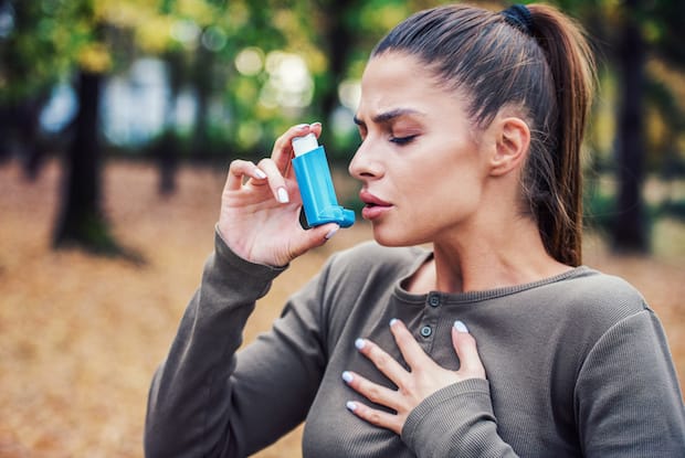 a woman using her quick-relief asthma inhaler