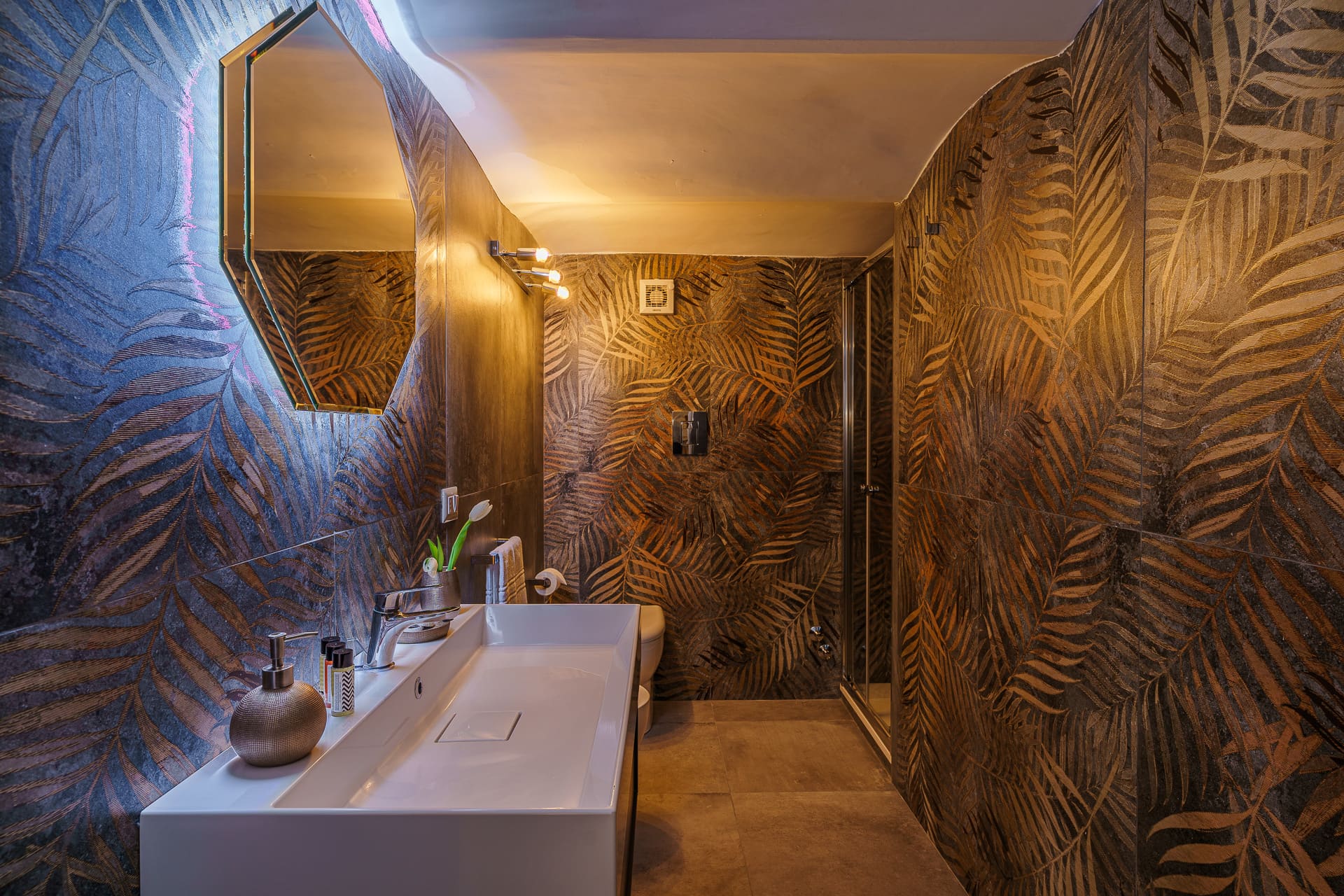 Lavabo e specchio ottagonale del bagno di design della suite Bella 'Mbriana con pareti a foglie di palma