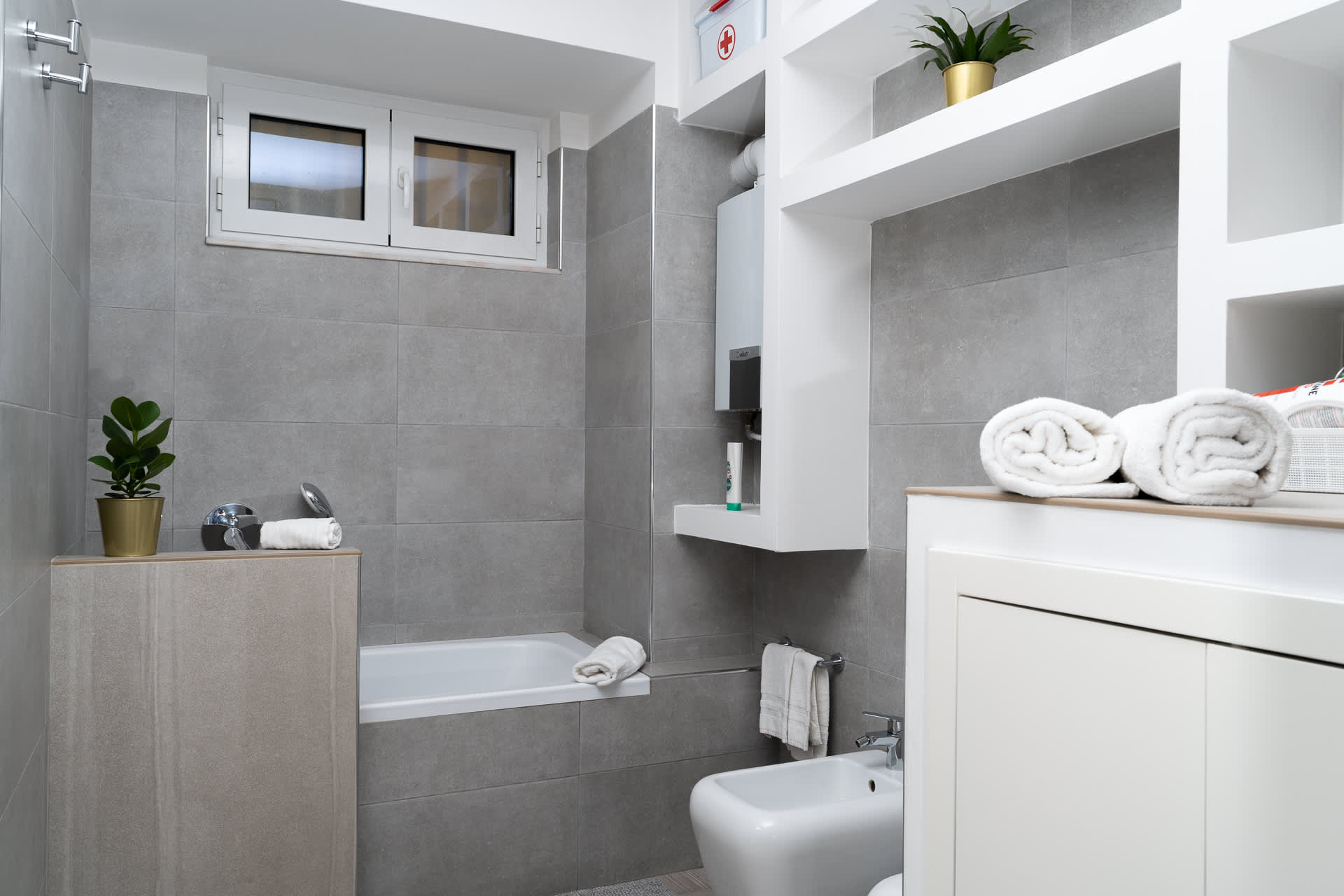 Bagno di Daymoon House Merliani con piastrelle grigie, vasca, finestra e asciugamani piegati