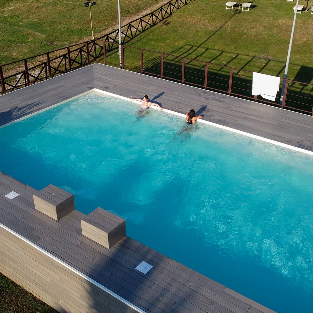 Piscina idromassaggio vista dall'alto, con acqua turchese in movimento e pedana in legno affacciata sul prato