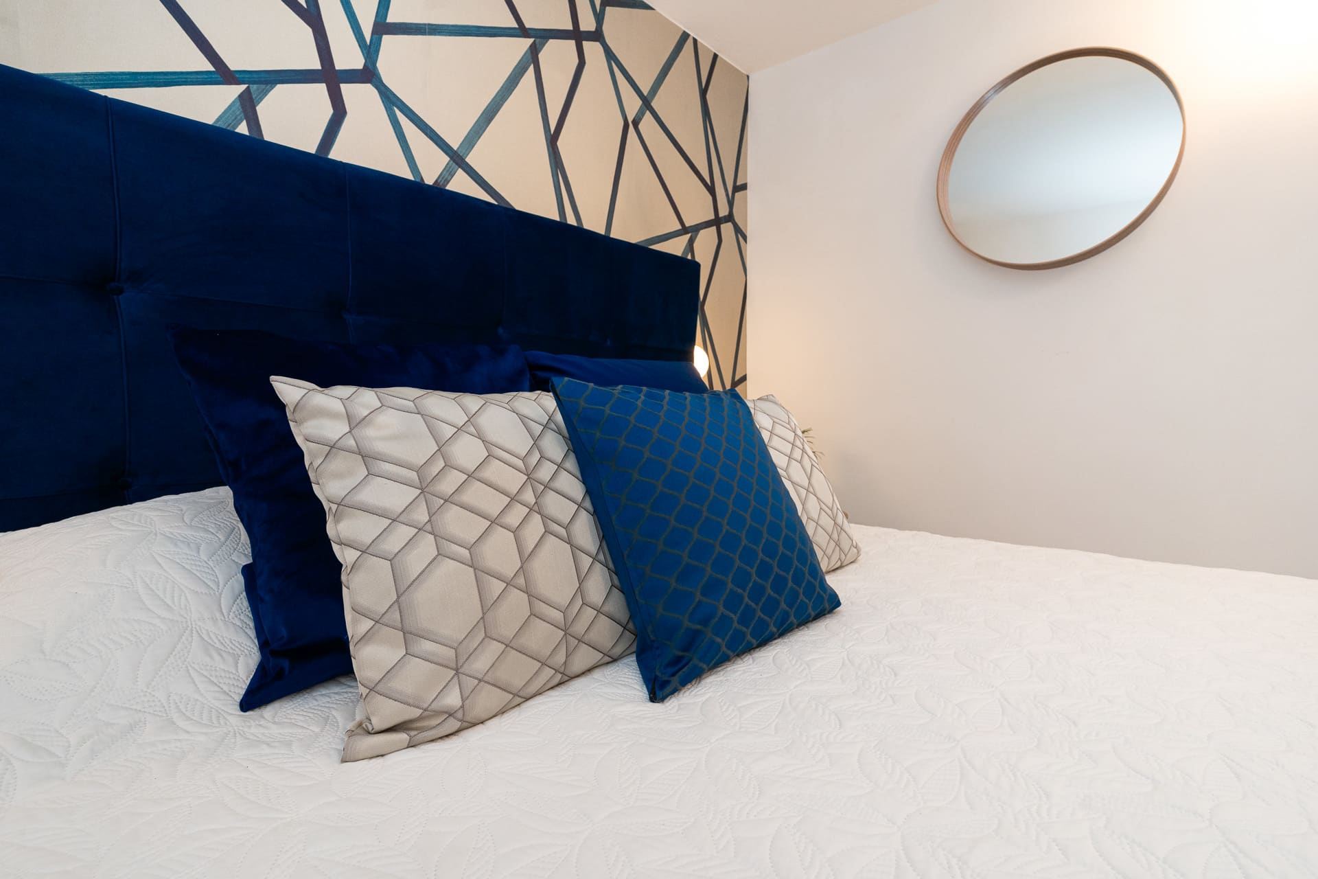 Cuscini decorativi e specchio tondo sul letto della camera Megaride