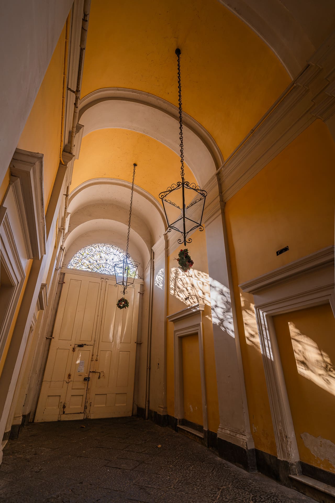 Androne storico del palazzo di Daymoon House Vanvitelli, con volta a botte color ocra e lanterne in ferro battuto