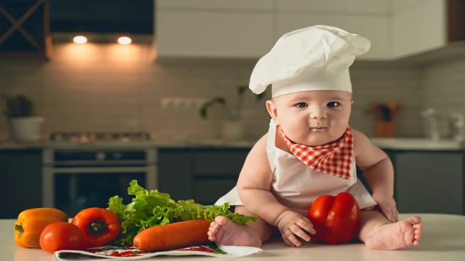 Cute baby dressed as a chef with food around him.