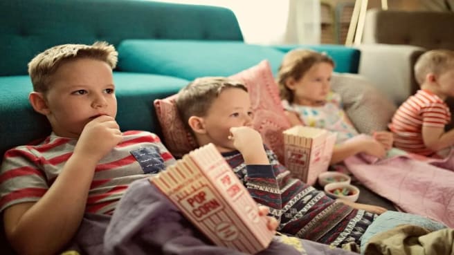 Four kids watching a kids' movie at home and eating popcorn.