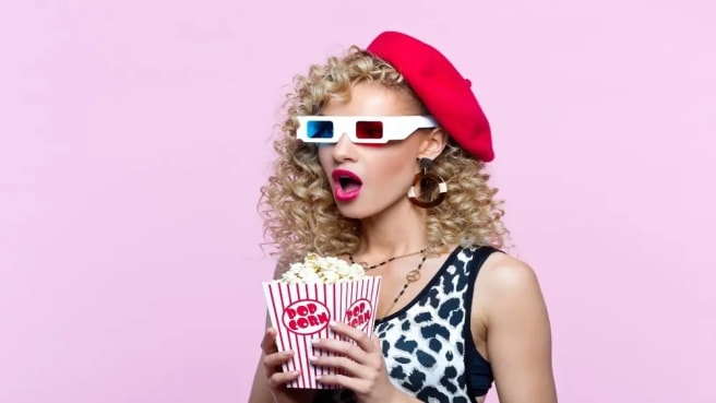 A woman dressed up in 1980s style watching movies and eating popcorn.