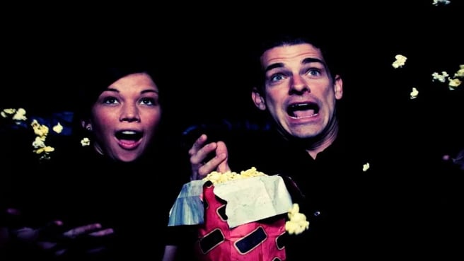 A couple watching a 90s movie and eating popcorn.