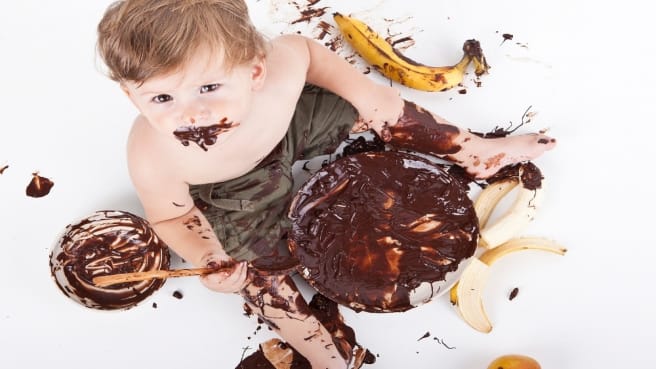 A baby eating chocolate with a big fun mess.