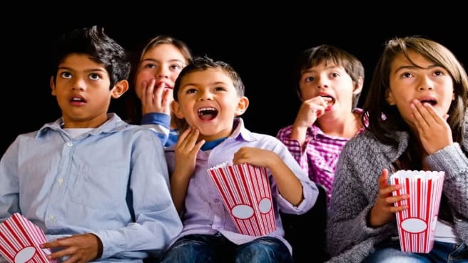 Five kids watching a kids' movie in the cinema and eating popcorn.