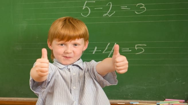 A redhead 4th-grade boy is thinking and looking on a green math chalkboard with thumbs up.