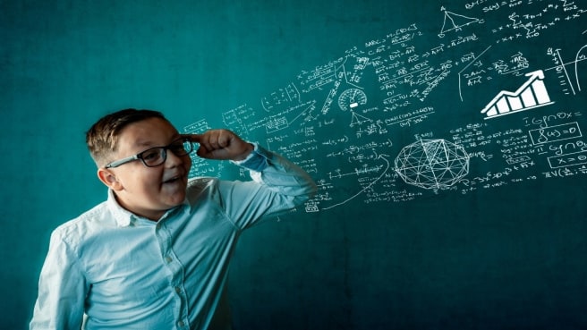 A funny 5th-grade boy is thinking and looking on a green math chalkboard.