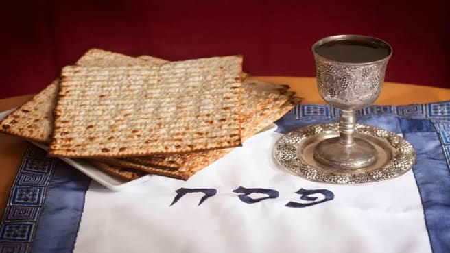 Matzah and wine on a white table cover with the wood Pesach in Hebrew.