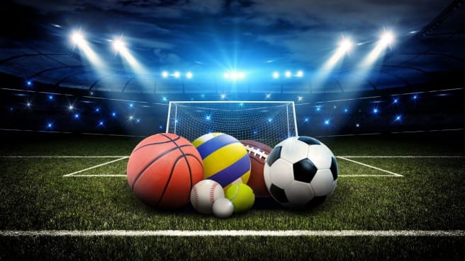 Popular sports balls on the grass in a middle of a sport stadium.
