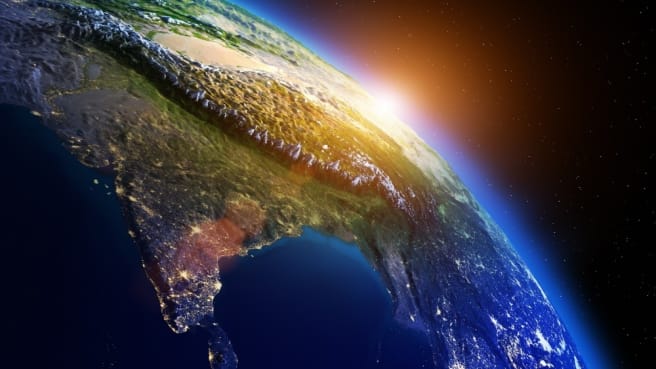 An image of the Earth from space, with the sun, is shining and glowing behind Earth.