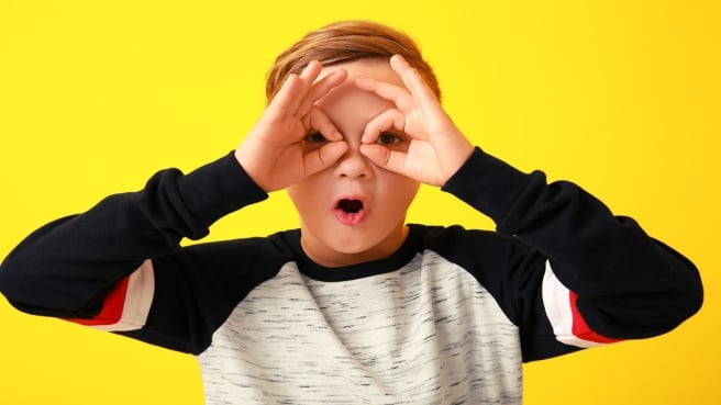A cute kid doing the shape of glasses with his hands on his face.