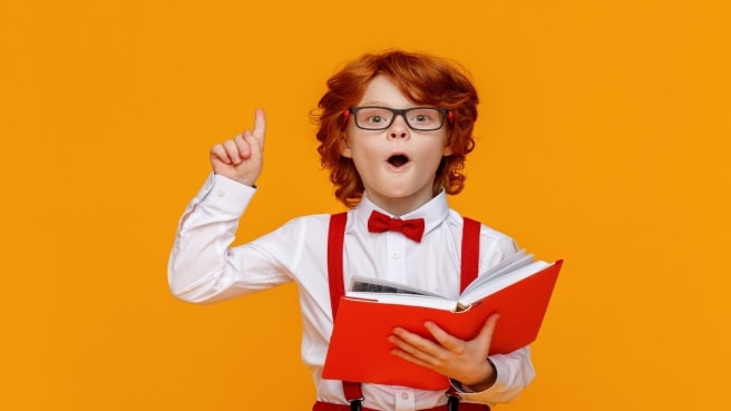 A cute kid with educational books, glasses, raising his finger in the air after he learned something.