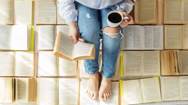 A woman reading a book on a floor with many books.