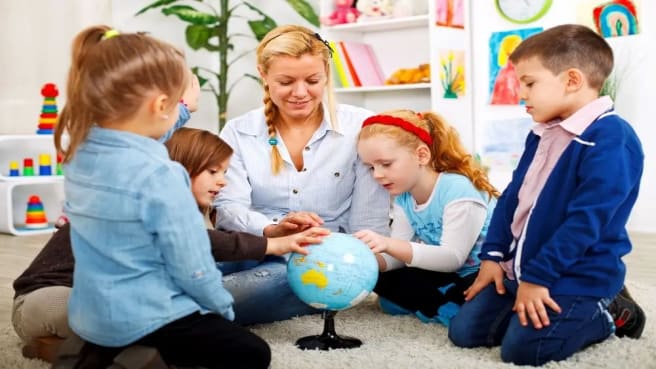 Kids and their geography teacher sitting on the floor and learning the Atlas.