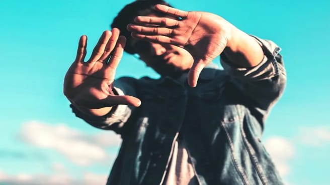 A handsome male celebrity hiding behind his hand.