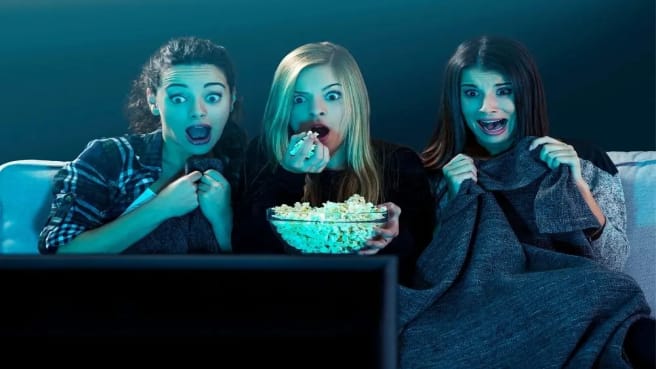 Three young girls sitting on a sofa and watching a movie with popcorn.