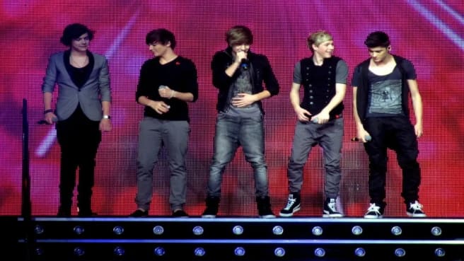 The entire members of One Direction on the stage with a pink background.