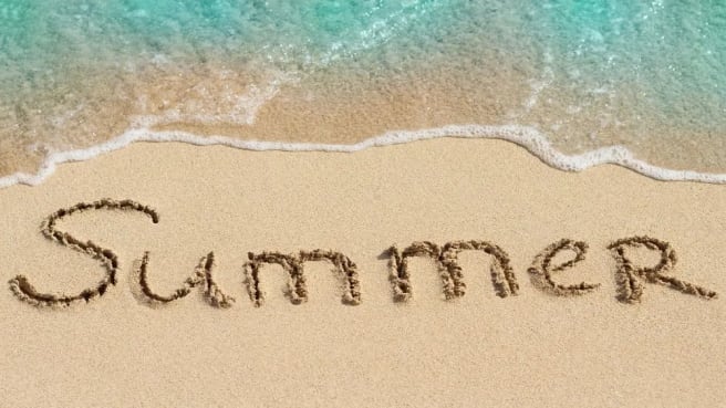 The word summer is written on the sand on the beach.